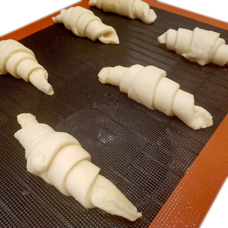 Gegangene Croissants auf der perforierten Backmatte Silpain